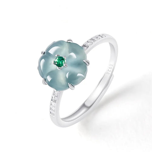 A silver ring featuring a flower-shaped light blue jadeite gemstone with a small green emerald at its center, set on a white background.