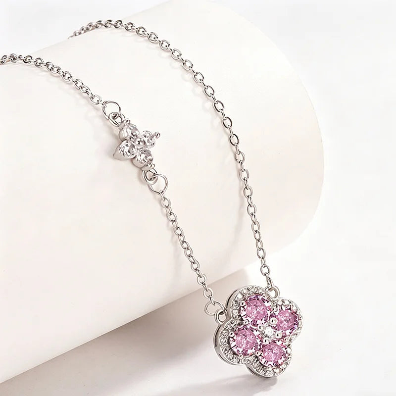 A silver-tone chain necklace with a flower-shaped pendant set with pink and clear crystals, displayed on a white curved jewelry stand.