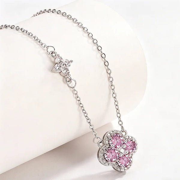 A silver-tone chain necklace with a flower-shaped pendant set with pink and clear crystals, displayed on a white curved jewelry stand.