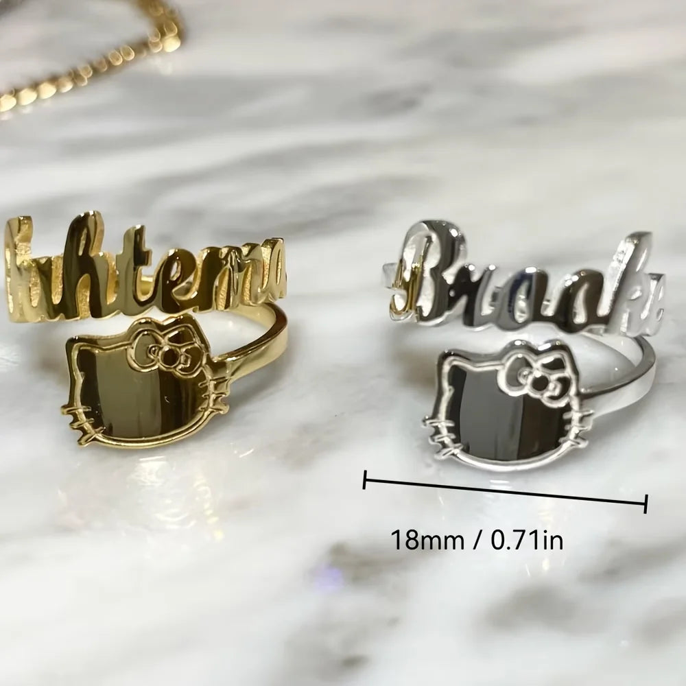 Two custom name and Hello Kitty ring options shown on a white marble surface, with one gold-toned ring and one silver-toned ring, and a dimension line indicating the width is 18mm (0.71 inches).