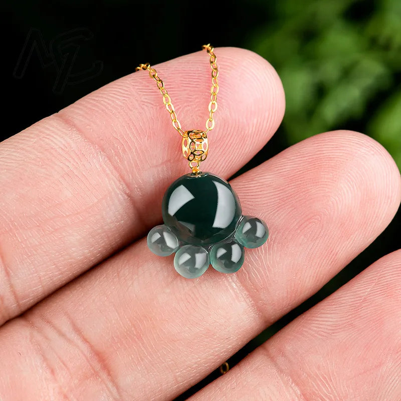 Green gemstone pendant on a gold chain held in a hand with a blurred green background